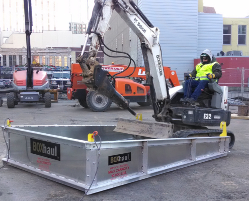 crane attached dump box being cleared by a man on heavy equipment
