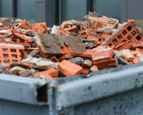 Red bricks debris in construction metal waste container close up. Building demolition