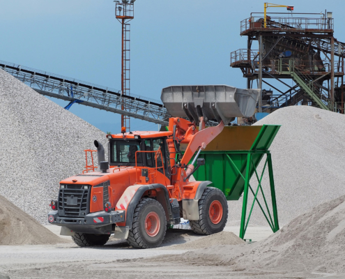 Red bulldozer at work on a green hopper under the conveyor belts in a gravel pit