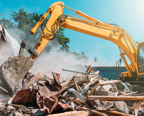 Demolition of building. Excavator breaks old house with dump box in background