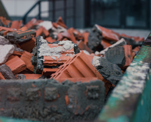 Green metal skip bin full of broken brick and stone material on construction site